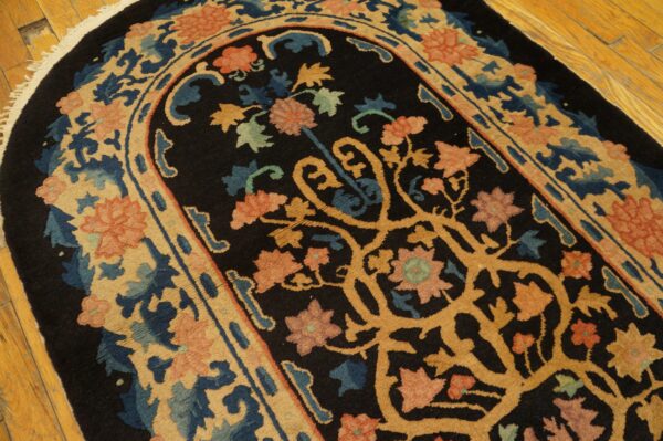 Ornate black rug with a curvilinear gold vine pattern and floral motifs in coral, blue, and tan on wood planks.