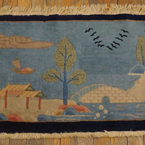 Blue runner rug with an olive green and tan landscape design of boats, trees, and architecture on wood flooring.