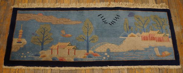 Blue runner rug with an olive green and tan landscape design of boats, trees, and architecture on wood flooring.