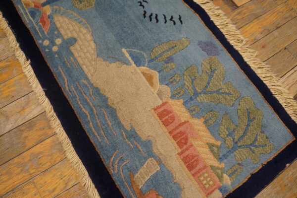 Low-pile blue rug with sculpted tan, green, and pink scenic elements, bordered in navy on distressed wood.
