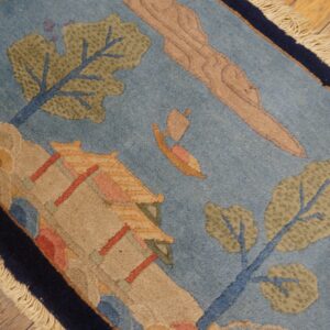 Light blue rug with a scenic pattern of green trees, beige architecture, and a sailboat on wood floors.