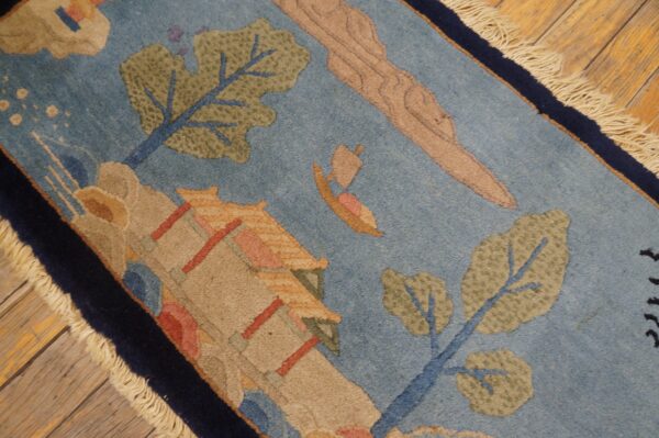 Light blue rug with a scenic pattern of green trees, beige architecture, and a sailboat on wood floors.