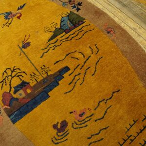 A gold and brown oval rug displaying a scenic pattern rests on light distressed wood flooring.