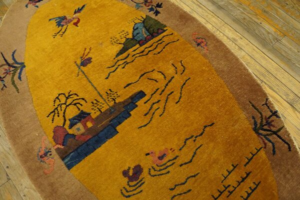A gold and brown oval rug displaying a scenic pattern rests on light distressed wood flooring.