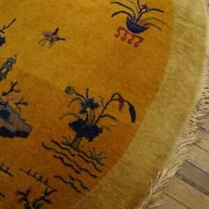 Circular yellow and olive rug with a scenic pattern and long fringe rests on rustic plank flooring.