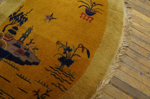 Circular yellow and olive rug with a scenic pattern and long fringe rests on rustic plank flooring.