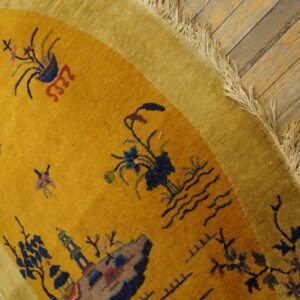 Gold rug detail showing a stylized landscape pattern, lighter yellow border, and fringe over wood flooring.