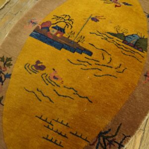 Oval yellow rug with a scenic pattern and brown floral border rests on distressed wooden floorboards.
