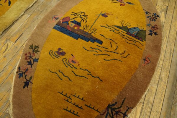 Oval yellow rug with a scenic pattern and brown floral border rests on distressed wooden floorboards.