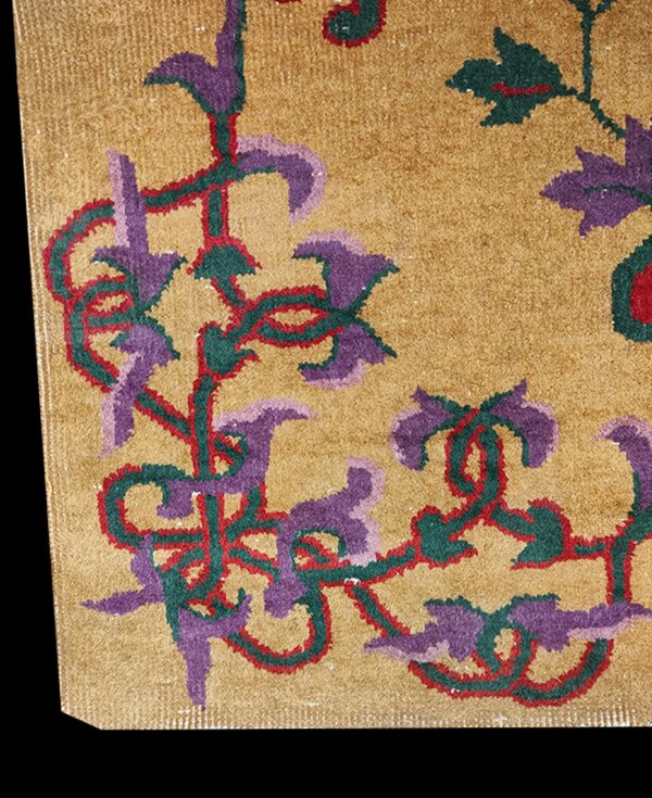 Rug close-up showing gold pile with scrolling floral motifs in purple, teal, and red.