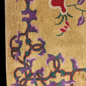 Textured gold rug detail with deep pile and bold purple, red, and green floral designs.