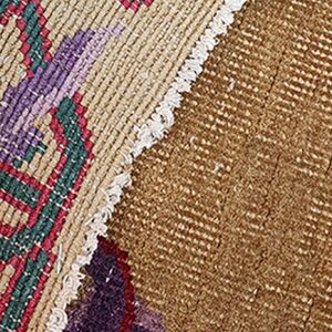 Detail of a brown, red, green, and purple patterned rug showing two textures joined by fringe.