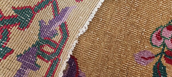 Detail of a brown, red, green, and purple patterned rug showing two textures joined by fringe.