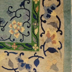 Teal and beige rug corner featuring sculpted floral and vine motifs with green accents on wood floor.