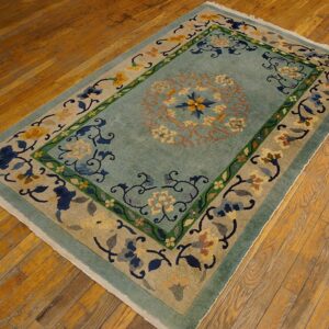 A rectangular rug featuring a pale blue field and ornate multicolored floral borders rests on a wooden plank floor.
