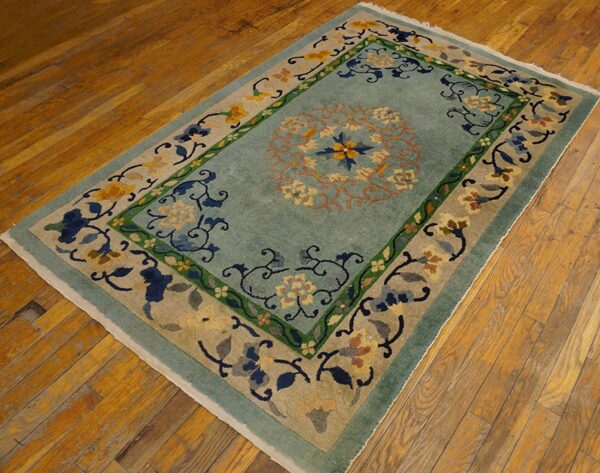 A rectangular rug featuring a pale blue field and ornate multicolored floral borders rests on a wooden plank floor.