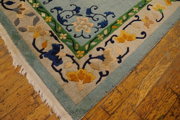 Light blue floral rug with beige, yellow, and green borders rests on rustic wood flooring, showing fringe.