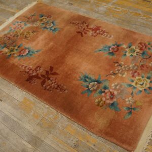 Coral-orange rug with scattered blue, pink, and yellow floral designs rests on weathered plank flooring.