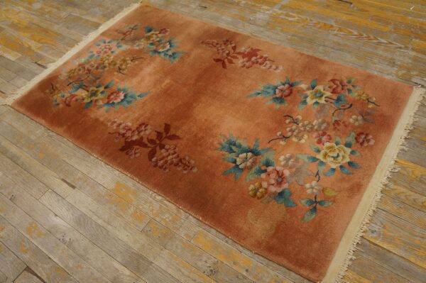 Coral-orange rug with scattered blue, pink, and yellow floral designs rests on weathered plank flooring.