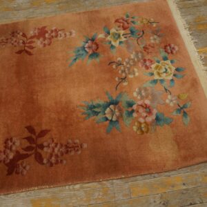 Pink-orange rug featuring colorful floral motifs rests on worn, yellow-toned wooden floors.