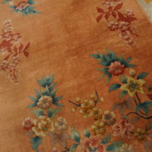 Salmon-colored high-pile rug with red, yellow, and teal floral patterns on distressed light hardwood.