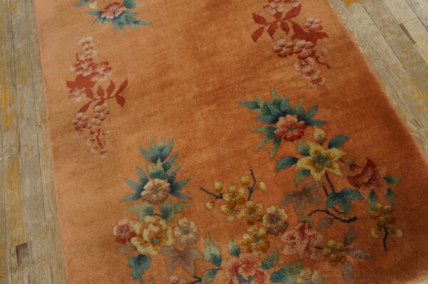 Salmon-colored high-pile rug with red, yellow, and teal floral patterns on distressed light hardwood.