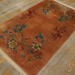 Rust-colored rug with off-white fringe and scattered floral designs on worn, yellow-painted wood planks.