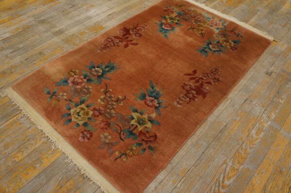 Rust-colored rug with off-white fringe and scattered floral designs on worn, yellow-painted wood planks.