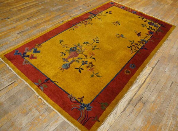 Mustard yellow rug features a red border and blue floral vase pattern on distressed wood floors.