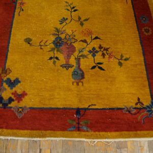 Floral motif rug in golden yellow and rust red colors placed on worn wood flooring.