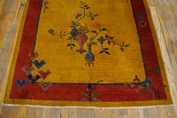 Floral motif rug in golden yellow and rust red colors placed on worn wood flooring.