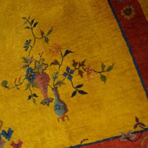 Mustard yellow rug with a red border and detailed floral vase motifs on distressed wood.