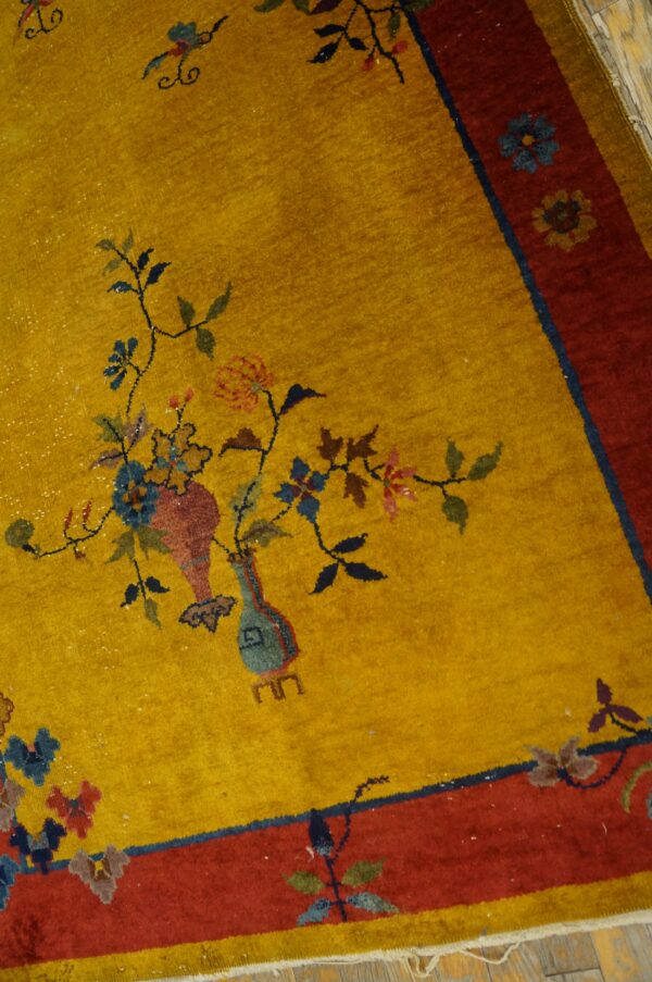 Mustard yellow rug with a red border and detailed floral vase motifs on distressed wood.