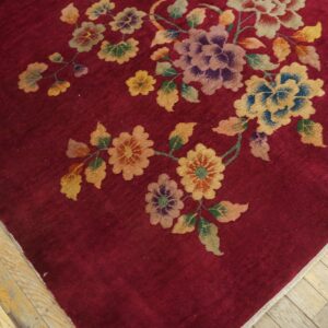 Deep red rug with sprawling colorful floral vine pattern sits on distressed blonde hardwood flooring.