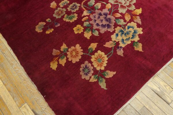 Deep red rug with sprawling colorful floral vine pattern sits on distressed blonde hardwood flooring.