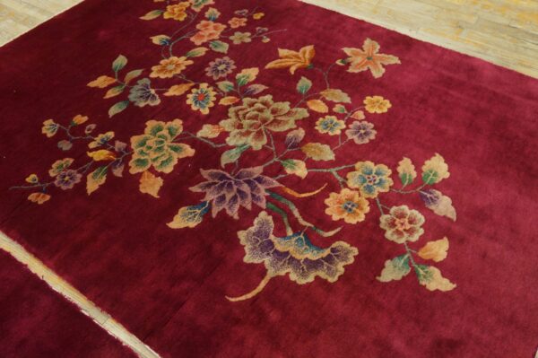 A crimson rug with colorful floral motifs rests on light, narrow plank wood flooring.