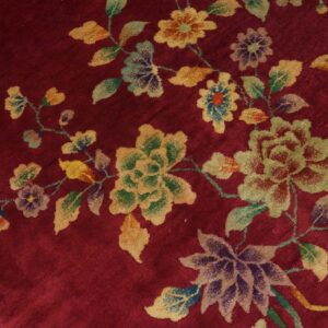 Plush red rug featuring a scattered multicolored floral pattern of yellow, green, and purple blooms.
