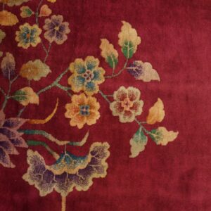 Plush red rug featuring a sprawling pattern of faded gold, green, and purple flowers on wood flooring.