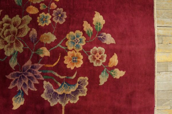 Plush red rug featuring a sprawling pattern of faded gold, green, and purple flowers on wood flooring.