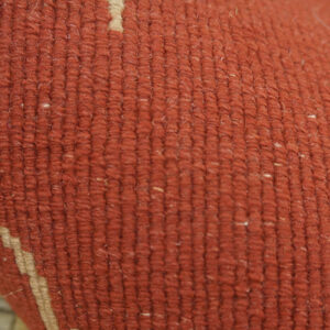 Detail view of a dense, rust-colored rug surface with subtle cream geometric and blurred pink patterns.