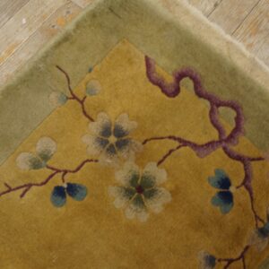 Gold rug corner featuring a floral branch pattern and olive border rests on light, distressed wood planks.