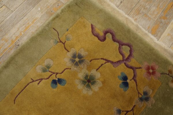 Gold rug corner featuring a floral branch pattern and olive border rests on light, distressed wood planks.