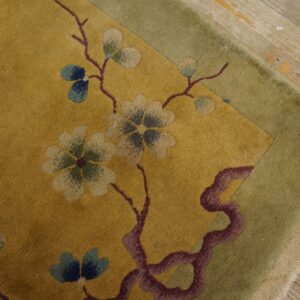 Gold rug with stylized floral pattern and moss green border resting on weathered wood floorboards.