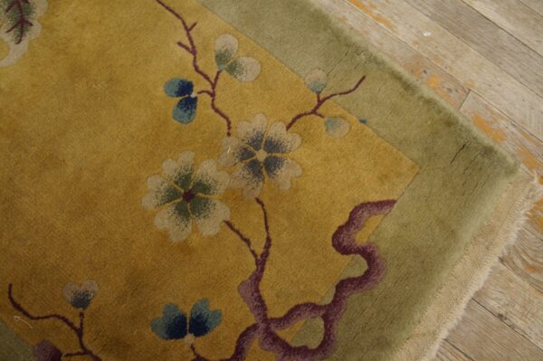 Gold rug with stylized floral pattern and moss green border resting on weathered wood floorboards.