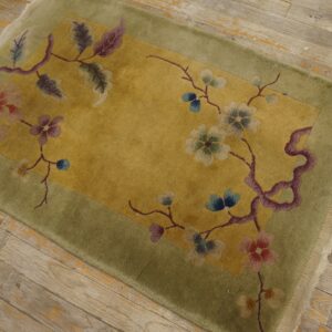 Plush green and yellow rug with a colorful floral vine pattern sits on distressed light wood planks.