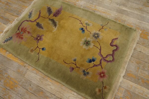 Plush green and yellow rug with a colorful floral vine pattern sits on distressed light wood planks.