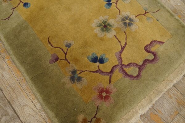 Gold and green rug featuring floral branches in blue and pink, resting on distressed wood planks.