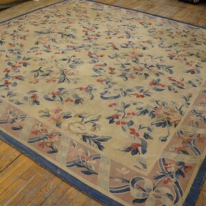 Cream rug with pink and blue ribbon and rose patterns on aged wooden plank flooring.