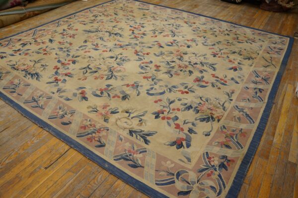 Cream rug with pink and blue ribbon and rose patterns on aged wooden plank flooring.