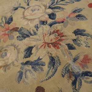 Textured close-up of a beige flat-weave rug featuring large floral designs in dusty blue, pink, and red.